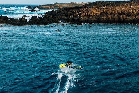 Duotone Skate D/LAB freestyle windsurf board during freestyle windsurfing at a rocky coastline