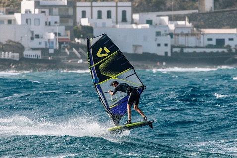 Duotone Idol freestyle windsurf sail during windsurfing action at a coastal location in dark teal and neon yellow