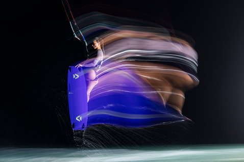 Tabla de kitesurf twin-tip Duotone Soleil SLS durante una sesión de kitesurf en agua oscura con efecto de luz en movimiento