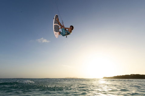 Tabla de kitesurf Duotone Blur SLS durante aéreo strapless al atardecer sobre el océano tropical