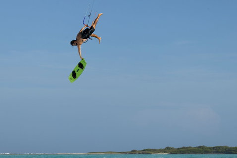 Planche de kitesurf twin-tip Duotone Entity Ergo en figure aérienne au-dessus d'une eau turquoise en vert citron