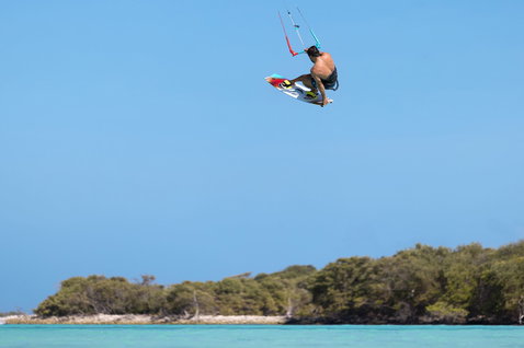 Planche de kitesurf twin-tip Duotone Vario lors d'un saut de kitesurf au-dessus d'un lagon tropical en bleu et blanc