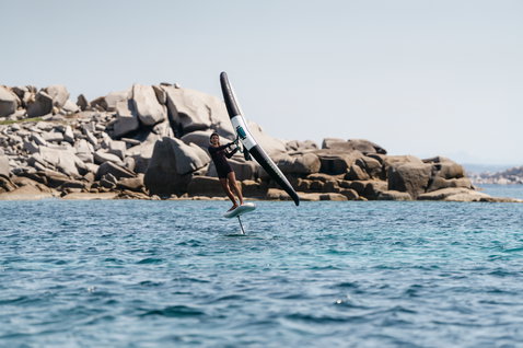 Duotone Skybrid Air foil board during wing foiling on the ocean with rocky coastline