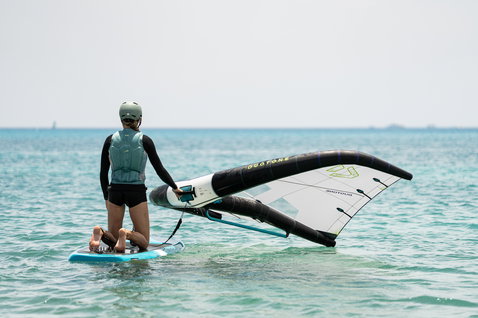Duotone Sky Start DST Foilboard beim Wing Foiling in flachem Ozeanwasser — Anfängerin kniet auf dem Board